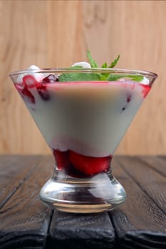 A glass of youghurt with marshmallow and raspberries decorated with mint leaves.