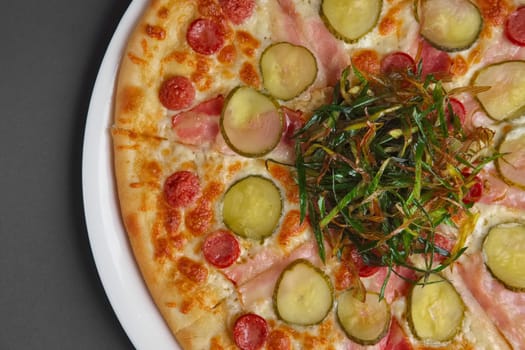 Top view of part of pizza with sausage, ham, bacon and pickled cucumber decorated with fried green onion