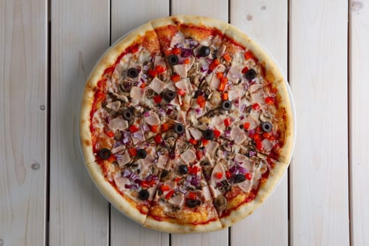 Top. view of pizza with ham, olives, pepper and mushroom on wooden table
