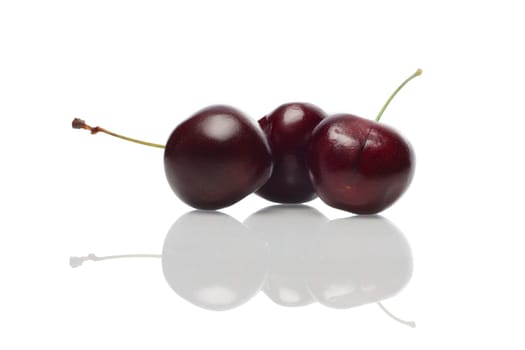 Three fresh cherries with reflection on glossy surface.