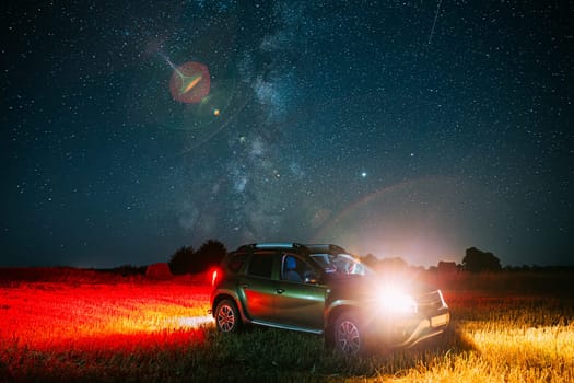 Night Starry Sky With Glowing Stars Above Car SUV In Countryside Landscape. Milky Way Galaxy And Rural Field Meadow