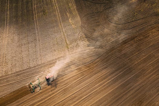 Aerial View. Tractor Plowing Field. Beginning Of Agricultural Spring Season. Cultivator Pulled By A Tractor In Countryside Rural Field Landscape. Dust Rises From Under Plows.