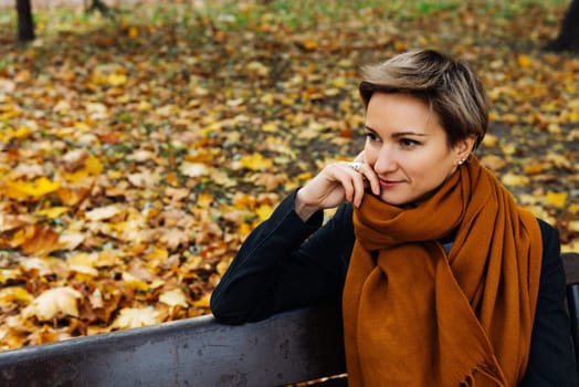 Portrait of a short-haired blonde in a terracotta scarf in an autumn park.