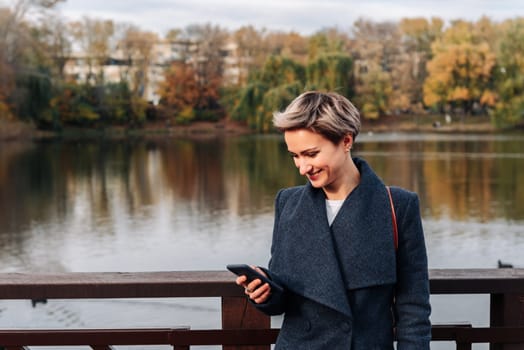 A woman in a city park by the river uses a smartphone.