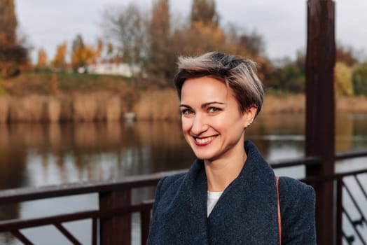 A woman smiles broadly near the river in autumn.