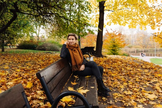 Short-haired blonde rests in an autumn park sitting on a bench.