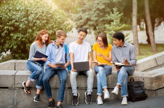 Chinese Student Guy Showing Educational Website On Laptop To Coursemates Sitting Outside. University Lifestyle Concept