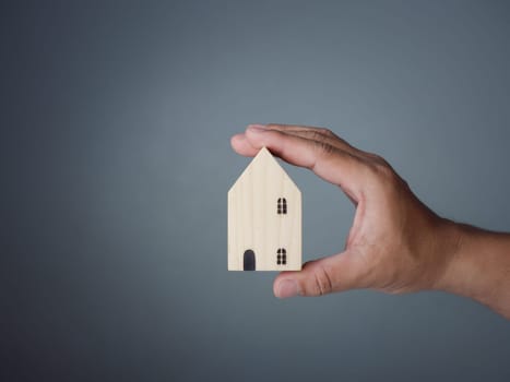 Concept of selling a house. A hand is holding a model house on a gray background. Real estate agent offer house, property insurance and security, affordable housing concepts, home insurance broker agent, salesman person.