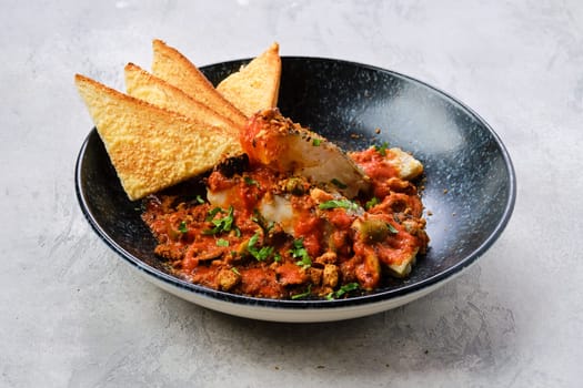 Fried zander served with steamed tomato, onion and olive sauce  on a plate