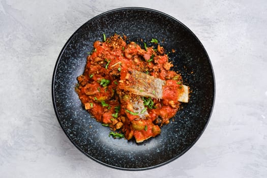 Top view of roasted zander served with steamed tomato, onion and olive sauce  on a plate
