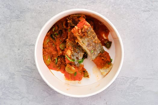 Top view of roasted zander served with steamed tomato, onion and olive sauce in take away cardboard package