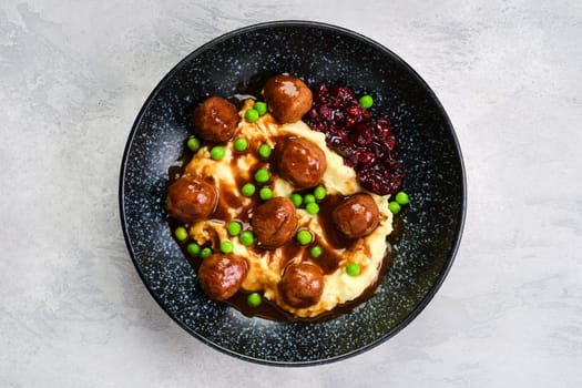 Top view of meatballs with gravy served with mashed potato, green pea and cranberry jam on a plate