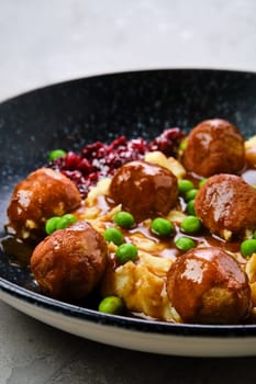 Closeup view of meatballs with gravy served with mashed potato, green pea and cranberry jam on a plate