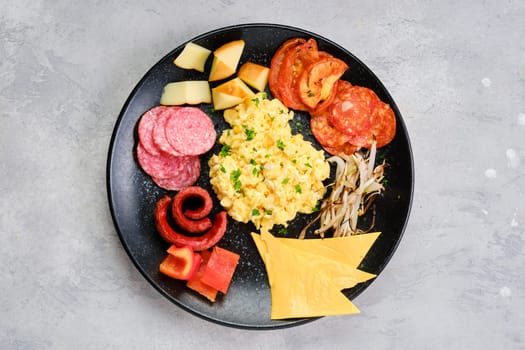 Top view of a plate with scrambled eggs with various sausages, cheddar cheese, bell pepper and roasted onion
