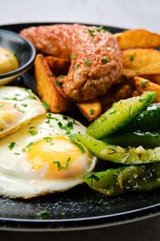 Closeup view of fried eggs with sausage, potato wedges and pickled cucumber