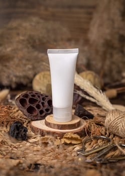 White plastic cosmetic tube on wood near natural decorations closeup, packaging mockup. Eco friendly skincare product, lotion or cream. Bohemian composition with dried leaves and flowers.