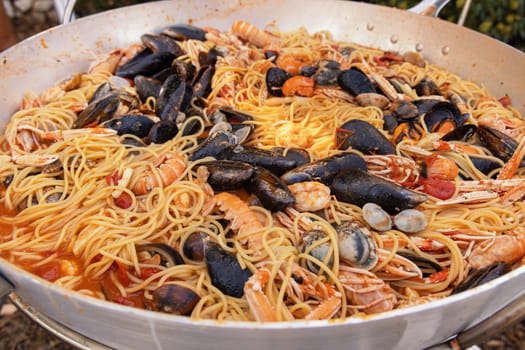 Italian spaghetti allo scoglio, pasta with seafood and tomatoes close up in a frying pan. Mediterranean Apulian traditional food with fresh stewed clams, shrimps, mussels, octopus and squid