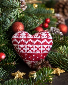Red knitted heart between decorations, fir branches and pine cones close up, mockup. Christmas or New Year greeting card template, Holiday or wedding stationery