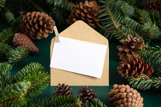 Blank card and envelope between fir branches and pine cones on green close up, mockup. Christmas or New Year greeting card template, Holiday winter composition