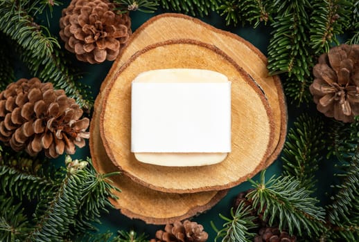 Natural soap bar between fir branches and pine cones on wooden piece top view. Brand package mockup. Health care concept. Handmade cosmetics. Winter concept