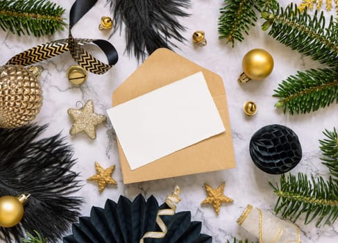 Paper card and envelope between black and golden Christmas decorations and fir tree branches top view. Winter flat lay with blank invitation card, Mockup, copy space