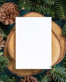 Vertical blank card between fir branches and pine cones on green top view mockup. Christmas or New Year greeting card template, Holiday winter composition