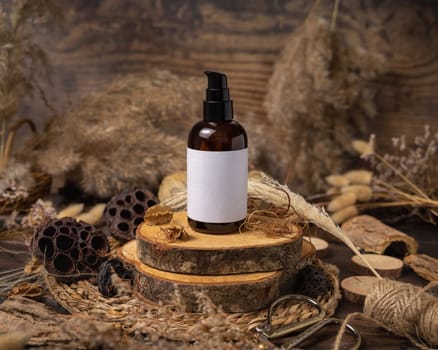 Glass one pump bottle on wood near natural boho decorations close up, label mockup. Skincare beauty product, lotion or essence. Bohemian eco friendly cosmetics flat lay with dried leaves.