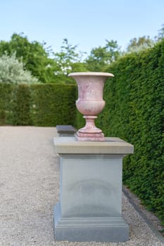 Vase on a pedestal as a decoration on a path in a very well-kept garden