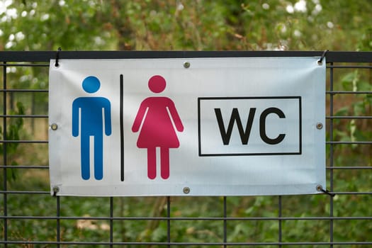 Indication of a nearby toilet by a sign on a fence in a park in Germany