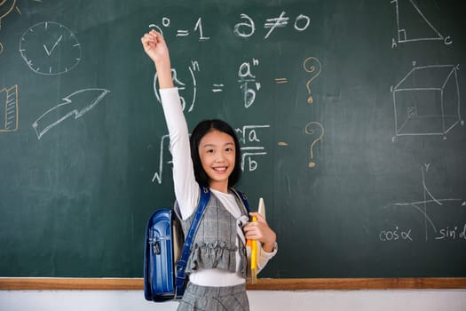 Education Back to school. Asian school girl in uniform on classroom raised arms to successful finished homework, primary child is standing front of class in school raised hands in win position