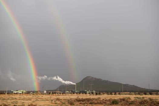 Double rainbow rising over an industrial area. Primary and secondary rainbows are visible