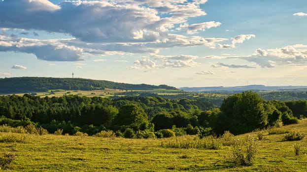 A sunny day in Saarland with a view over meadows into the valley. Some sunny clouds in the sky and cows grazing. A moment to linger, rest and enjoy