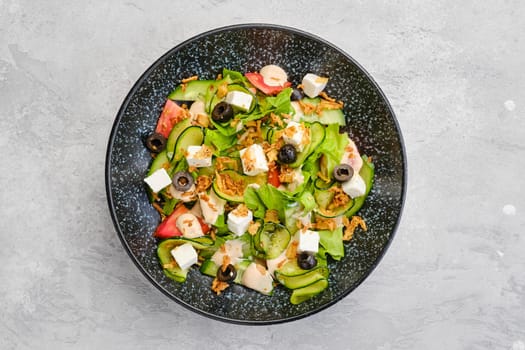 Top view of salad with lettuce, cucumber, olives, tomato, feta cheese and bacon chips