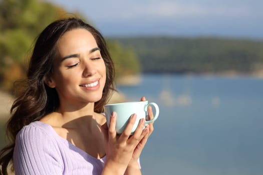 Happy woman enjoying holding coffee mug a sunny day in nature