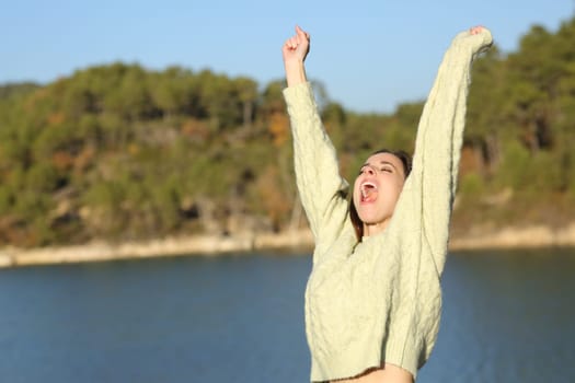 Excited woman in winter celebrating holiday raising arms in a lake