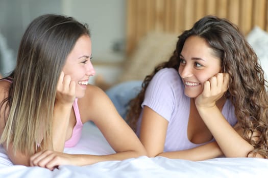 Two happy women looking each other lying on a bed in the bedroom