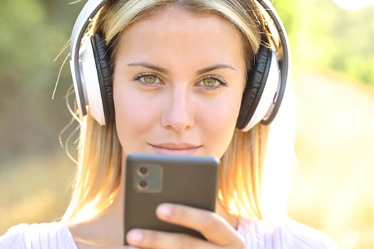 Front view portrait of a woman wearing wireless headphones holding smart phone looking at you