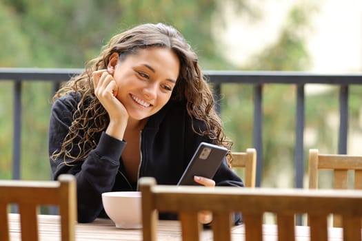 Happy woman in a balcony smiling using smart phone