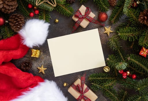 Paper card between Christmas decorations, wrapped gift boxes and green fir branches top view. Horizontal blank card mockup, flat lay, copy space. Christmas or New Year Holiday greeting card template