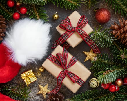 Wrapped gift boxes between Christmas decorations, Santa Claus hat and green fir branches top view on dark black background. Christmas or New Year Holiday atmosphere flat lay