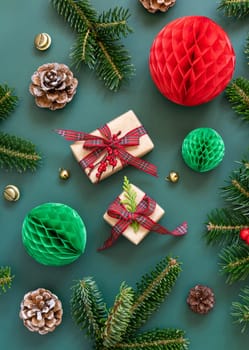 Wrapped gift boxes between Christmas decorations and green fir branches top view on green background. Christmas or New Year Holiday atmosphere flat lay