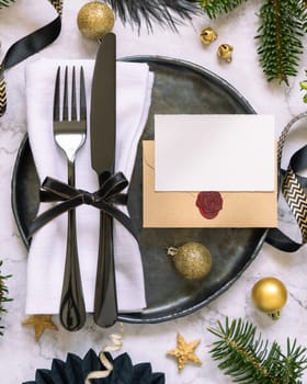 Black and golden Table setting with ornaments and fir tree branches top view, place card mockup. Christmas or New Year atmospheric composition flat lay, copy space.