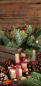 Wrapped gift boxes between Christmas decorations, pine cones and green fir branches close up on wooden background, copy space. Christmas or New Year Holiday atmosphere flat lay