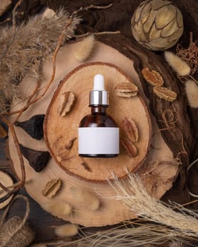 Glass dropper bottle on wood near natural boho decorations top view, label mockup. Skincare beauty product, serum or essence. Bohemian eco friendly cosmetics flat lay with dried leaves.