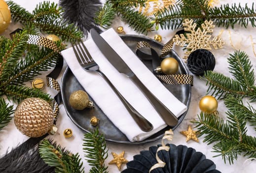 Black and golden Christmas table setting with decorations and fir tree branches close up. Winter table with fork, knife and plate. Winter New Year or Christmas dinner atmosphere