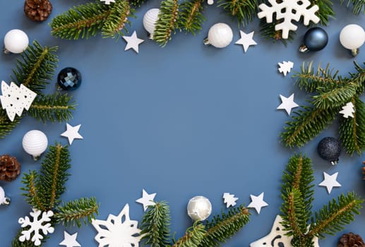 White Christmas decorations and fir tree branches on a blue top view with copy space. New Year and Christmas holiday atmospheric flat lay with baubles, snowflakes and stars