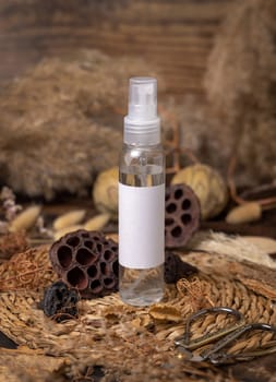 Transparent Refillable spray bottle on wood near natural boho decorations close up label mockup. Skincare beauty product, lotion or essence. Bohemian eco friendly cosmetics flat lay with dried leaves.