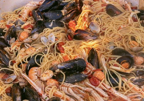 Italian spaghetti allo scoglio, pasta with seafood and tomatoes close up in a frying pan. Mediterranean Apulian traditional food with fresh stewed clams, shrimps, mussels, scampi, octopus and squid