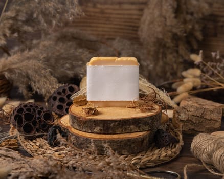 Handmade soap bar with blank label on wood near natural decorations close up, package mockup. Eco friendly skincare product. Bohemian composition with dried leaves and flowers.