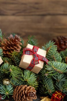 Wrapped gift boxes on reen fir branches near Christmas decorations and pine cones close up on wooden background, copy space. Christmas or New Year Holiday atmosphere